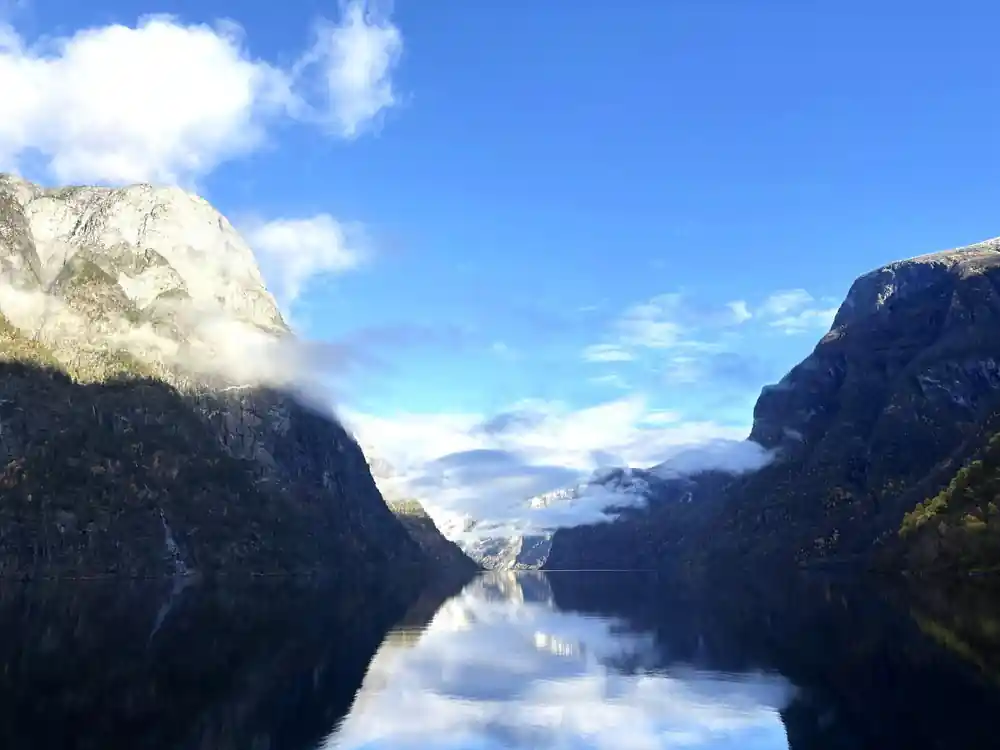 Cloud reflected in a mirror-flat fjord between steep walls