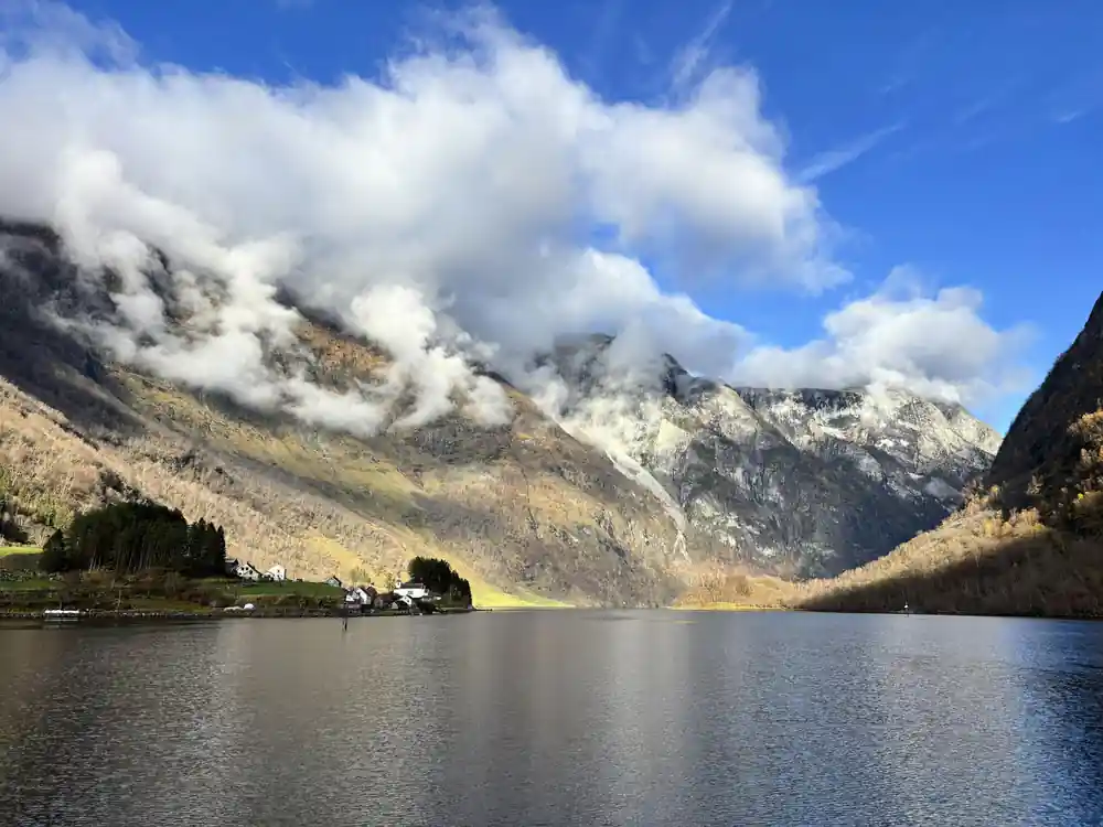 Cloud tearing across a dark mountain wall above still water