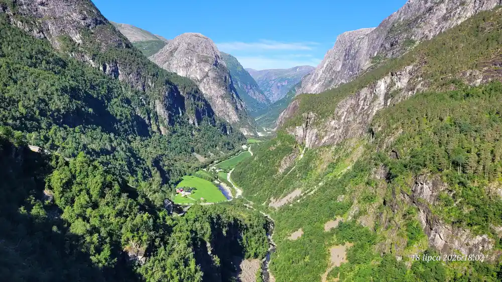 A green valley with farms and a waterfall on the wall behind