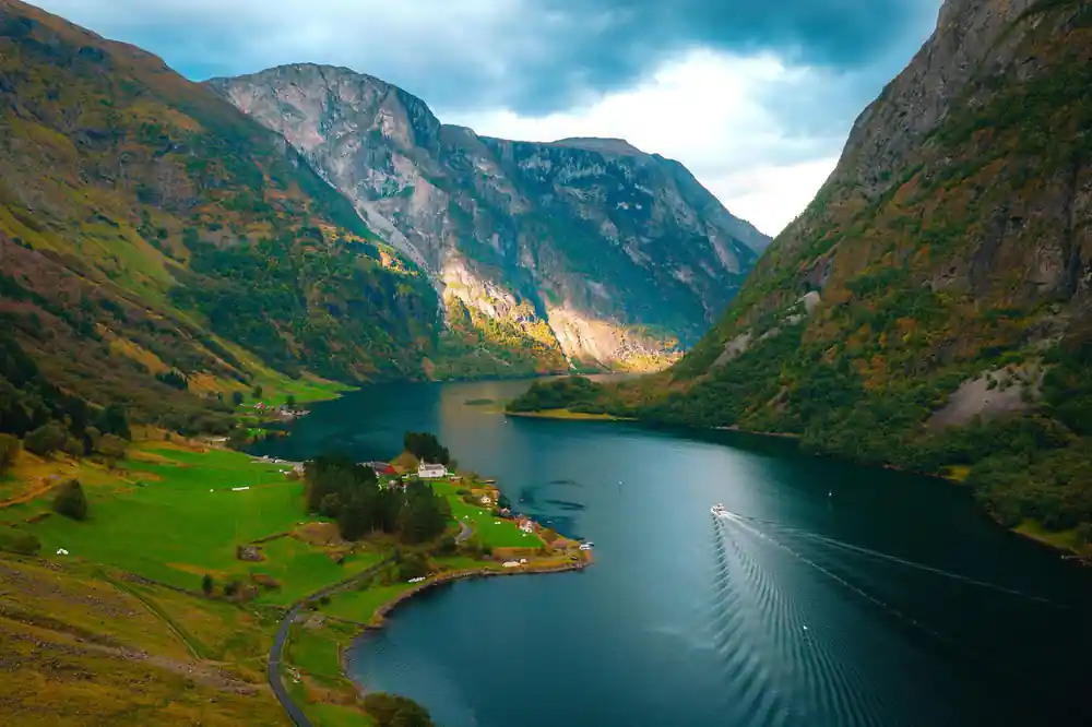 A green valley floor meeting the fjord with a boat wake on the water