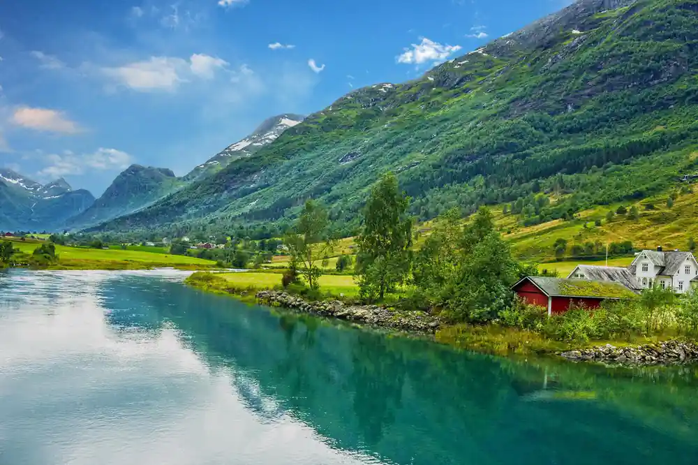 A red farm building beside turquoise water under a green mountain