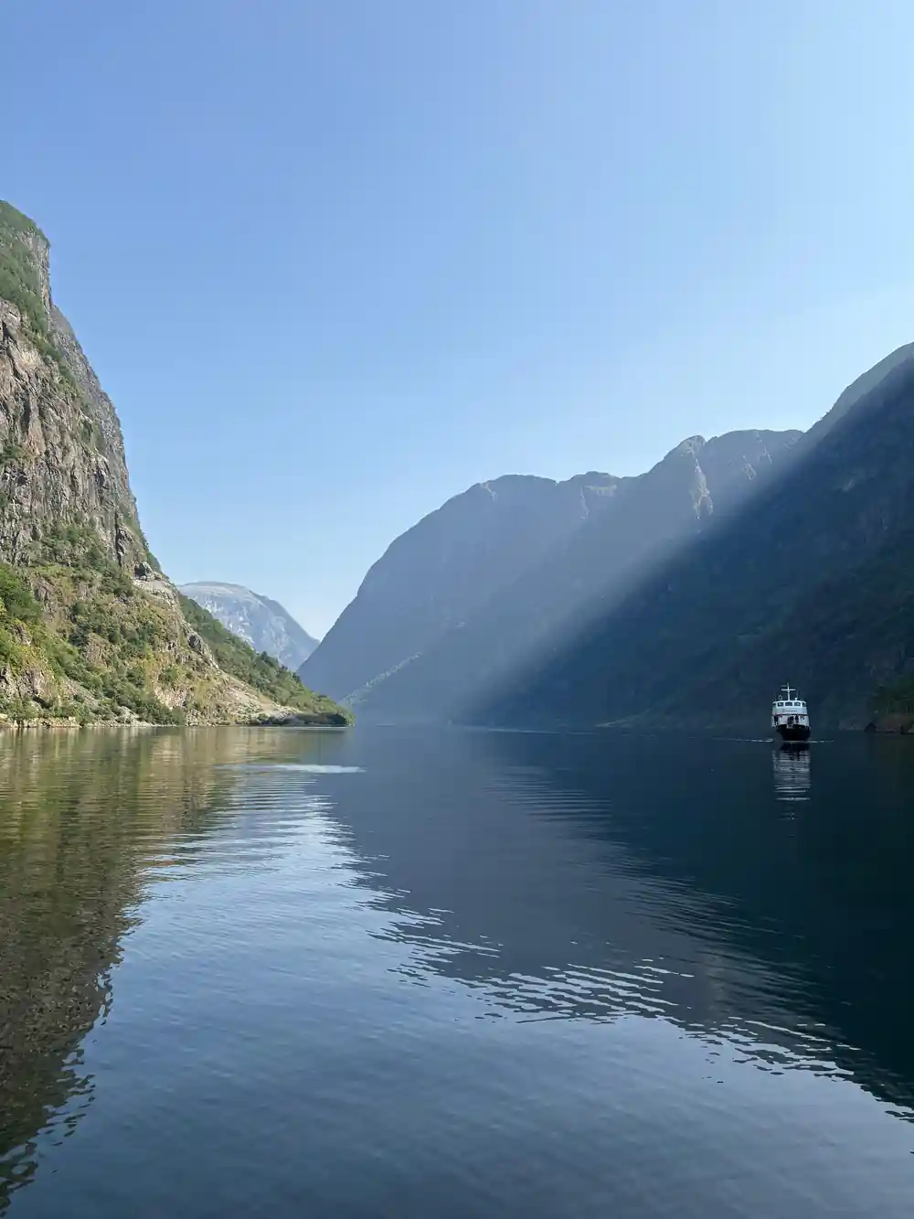 A small vessel far down a still fjord between two green walls