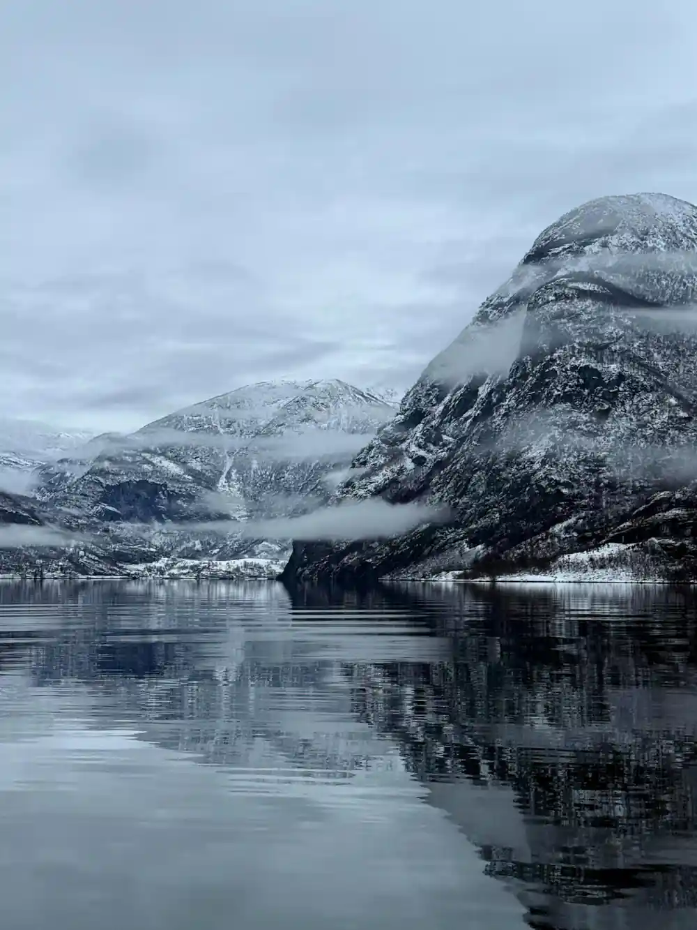 A snow-dusted fjord under low grey cloud in winter