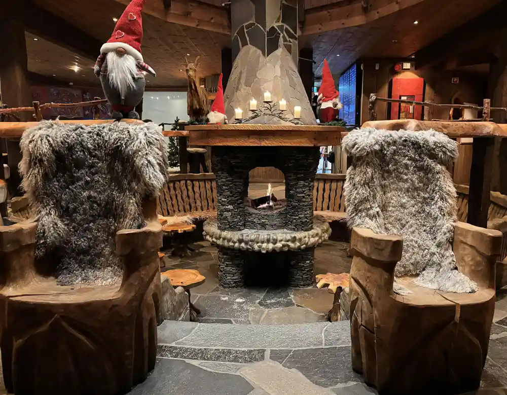 A stone fireplace and fur-covered chairs in a timber interior