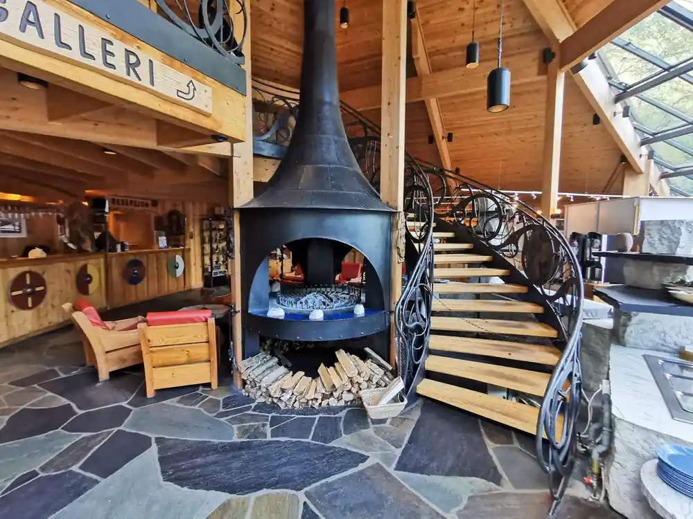 A tall black fireplace and a spiral stair inside a timber lodge