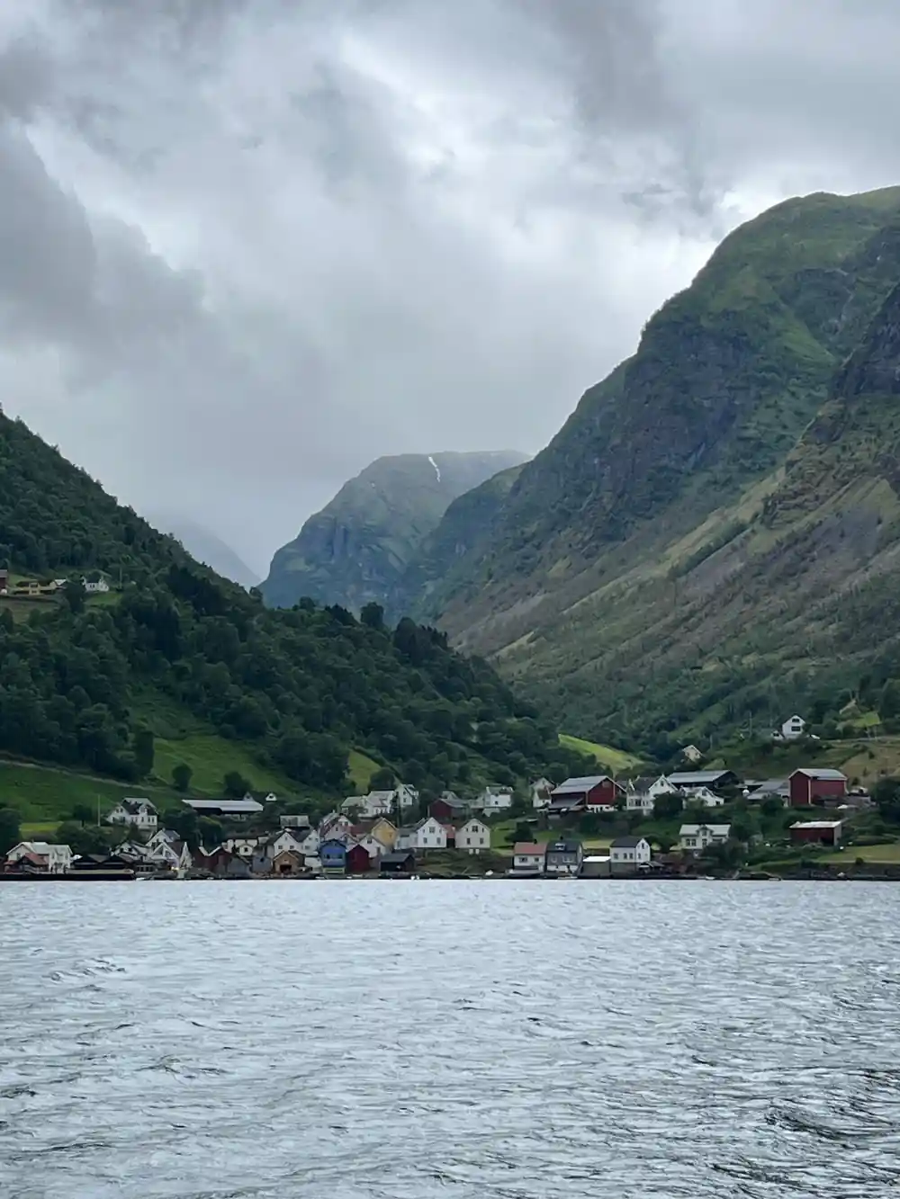 A village on the shore below a steep green mountain from the water