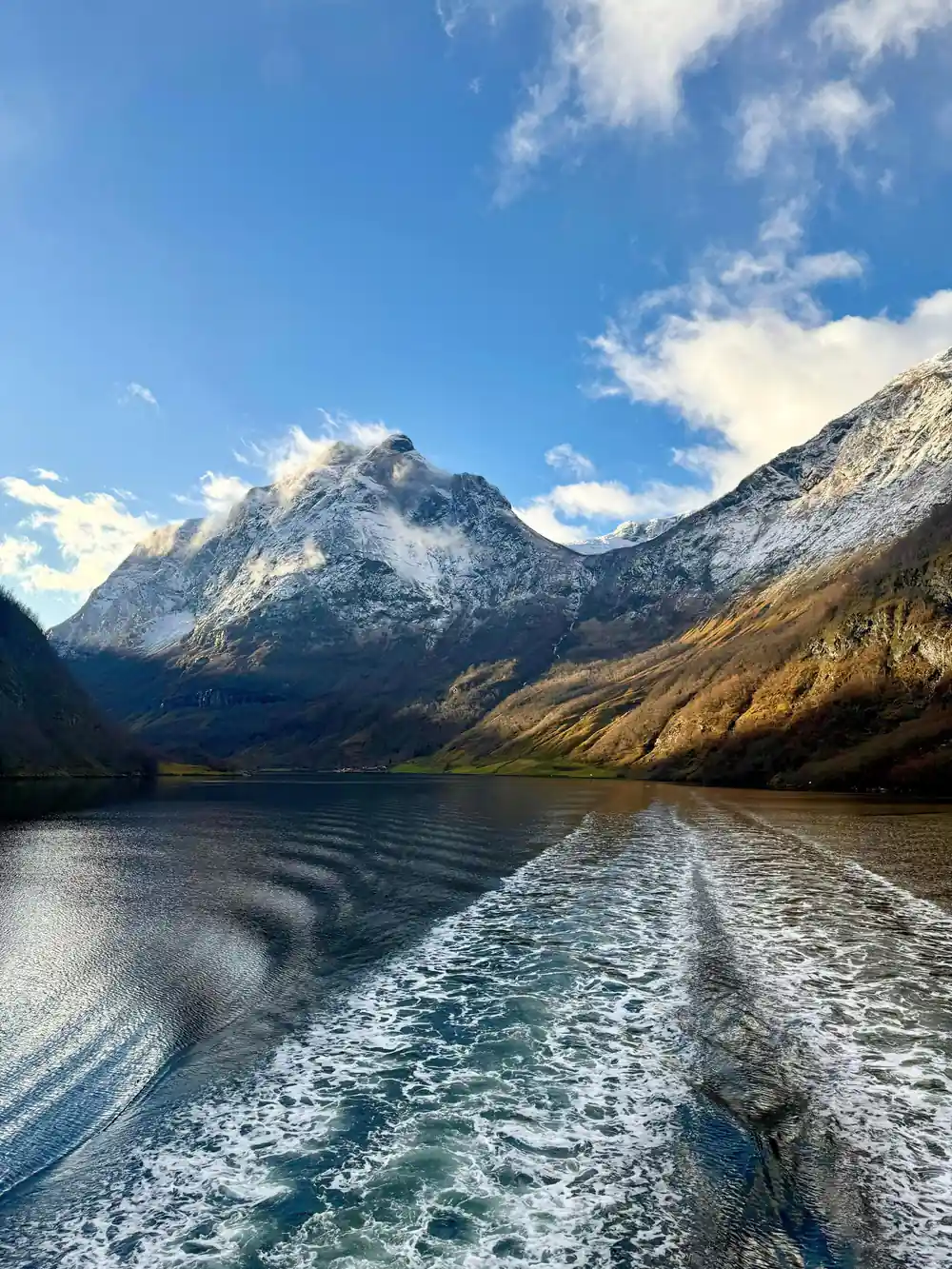 The wake of the boat spreading between snow-topped mountains